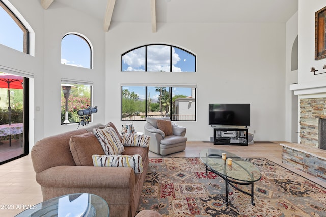 living room featuring high vaulted ceiling, light hardwood / wood-style flooring, beam ceiling, and a stone fireplace