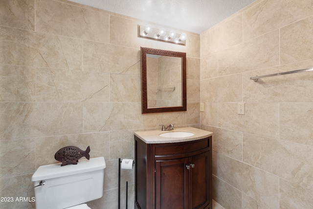 bathroom with tile walls, a textured ceiling, vanity with extensive cabinet space, and toilet