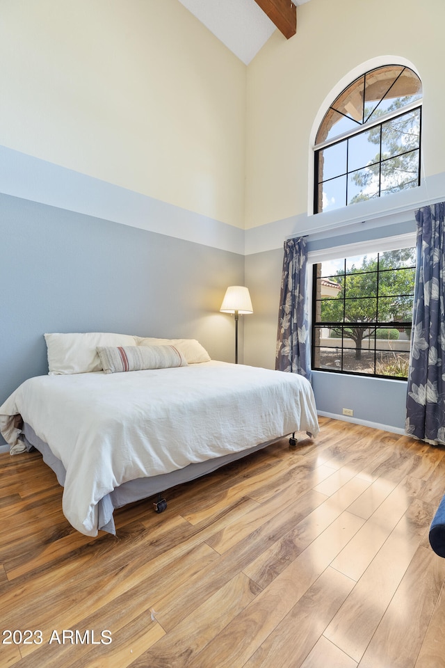 bedroom featuring high vaulted ceiling, light wood-type flooring, and beam ceiling