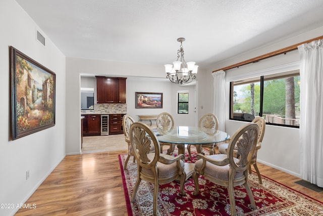 dining area featuring wine cooler, a notable chandelier, and light hardwood / wood-style flooring