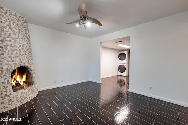 unfurnished living room with ceiling fan, a large fireplace, and stacked washer and clothes dryer