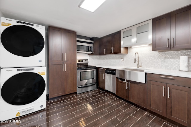 kitchen with appliances with stainless steel finishes, tasteful backsplash, stacked washing maching and dryer, dark brown cabinets, and sink