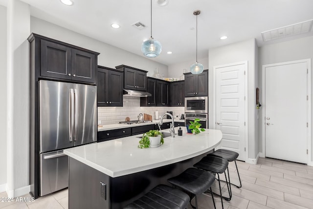 kitchen with a breakfast bar, a center island with sink, decorative light fixtures, and appliances with stainless steel finishes