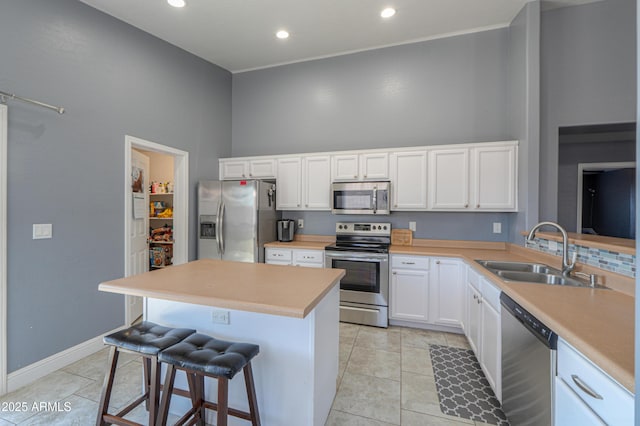 kitchen with sink, light tile patterned floors, appliances with stainless steel finishes, white cabinetry, and a kitchen bar