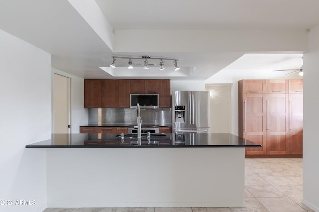 kitchen with sink, light tile patterned floors, a tray ceiling, kitchen peninsula, and stainless steel appliances