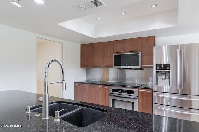 kitchen featuring a tray ceiling, sink, dark stone counters, and appliances with stainless steel finishes