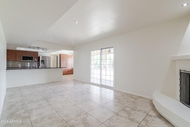 unfurnished living room featuring light tile patterned floors, sink, and track lighting