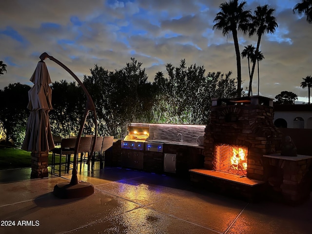 patio terrace at dusk with grilling area, area for grilling, exterior fireplace, and sink