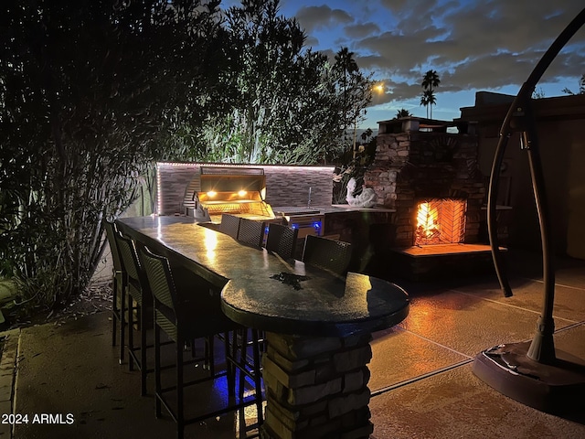 patio terrace at dusk featuring area for grilling, exterior bar, and an outdoor kitchen