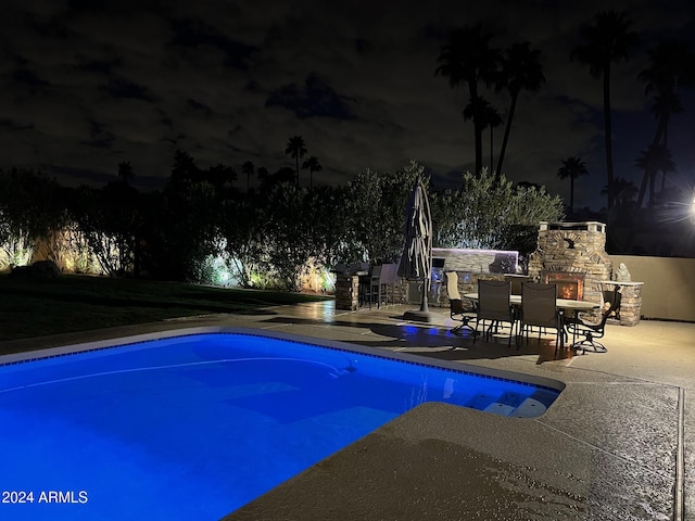 pool at night featuring an outdoor stone fireplace and a patio