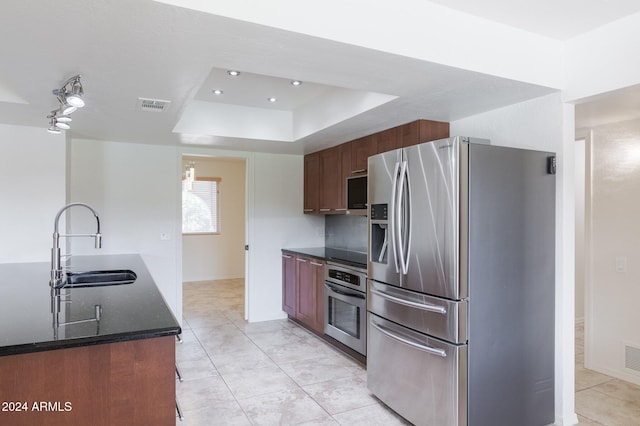 kitchen with a tray ceiling, sink, light tile patterned floors, and appliances with stainless steel finishes