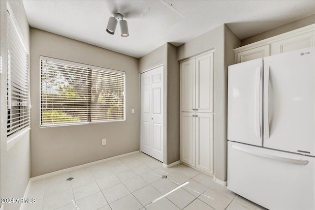 kitchen with white cabinets, a textured ceiling, white fridge, and light tile patterned floors