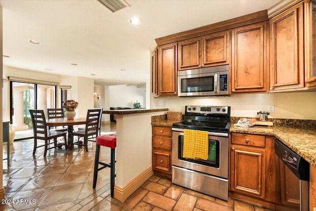 kitchen with stainless steel appliances, dark stone counters, kitchen peninsula, and a kitchen breakfast bar