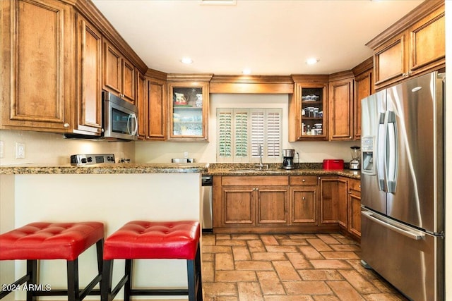 8638 E Paraiso Dr, Scottsdale, AZ 85255 - kitchen featuring a breakfast bar area, brick floor, brown cabinets, a sink, and stainless steel appliances