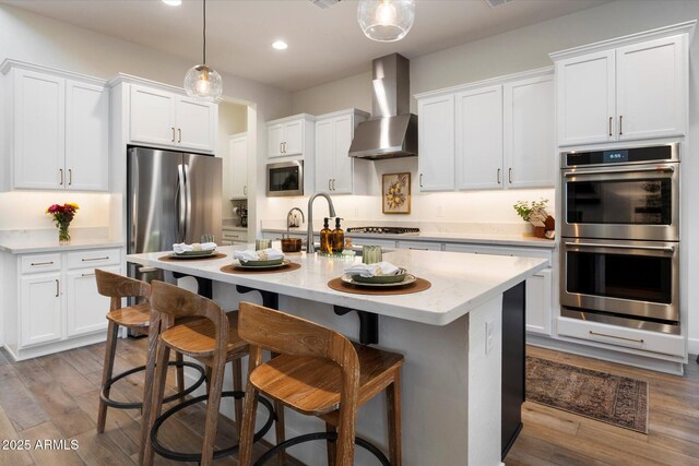 5661 S Dante, Mesa, AZ 85212 - kitchen with stainless steel appliances, wall chimney exhaust hood, an island with sink, white cabinets, and recessed lighting