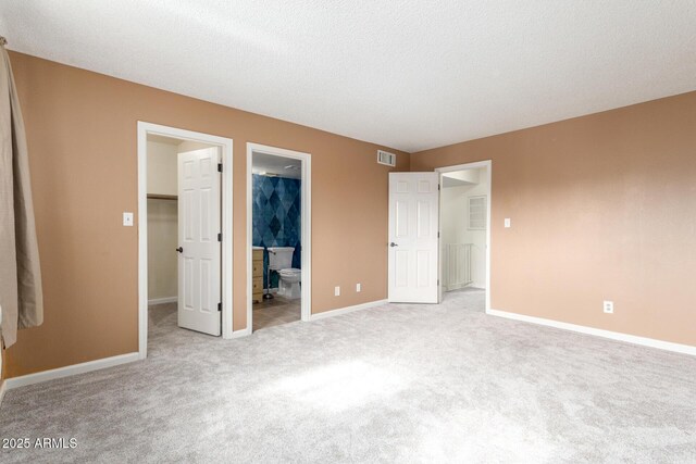 unfurnished bedroom with light carpet, ensuite bath, a walk in closet, and a closet