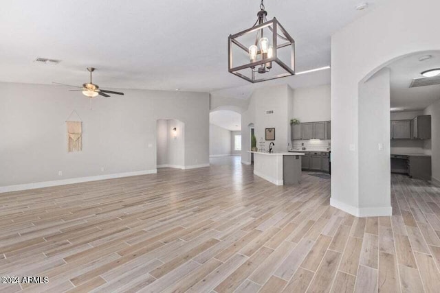 unfurnished living room with ceiling fan with notable chandelier and light hardwood / wood-style floors