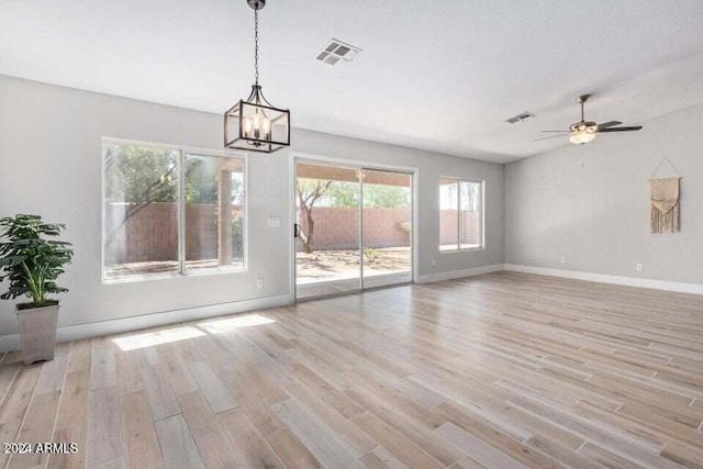 unfurnished dining area featuring ceiling fan with notable chandelier and light hardwood / wood-style floors