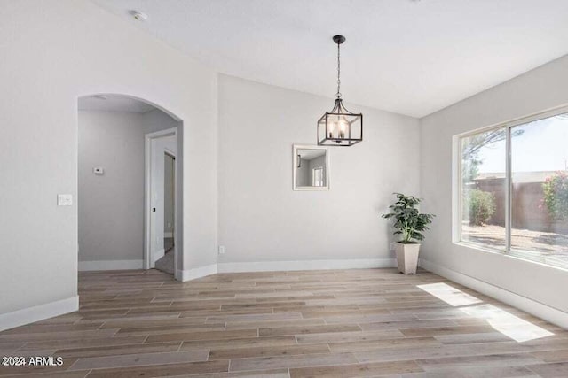 unfurnished dining area with wood-type flooring, vaulted ceiling, and an inviting chandelier