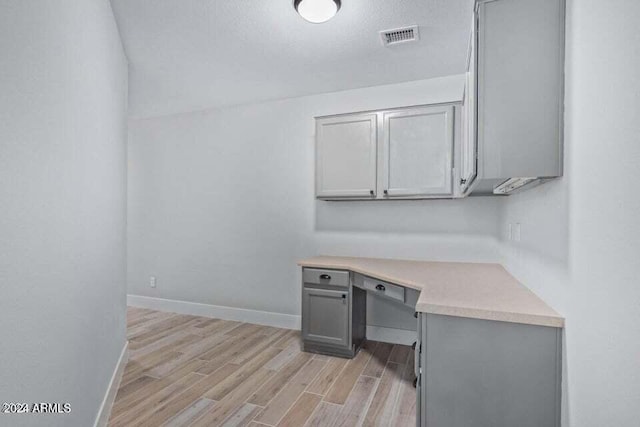 unfurnished office featuring a textured ceiling, built in desk, and light hardwood / wood-style flooring