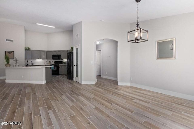 kitchen with hanging light fixtures, a notable chandelier, light hardwood / wood-style floors, gray cabinets, and black appliances