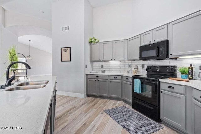 kitchen with light wood-type flooring, tasteful backsplash, sink, black appliances, and high vaulted ceiling