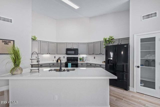 kitchen featuring black appliances, sink, a high ceiling, and light hardwood / wood-style flooring