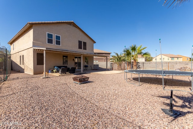 back of house with a trampoline, an outdoor living space with a fire pit, and a patio area