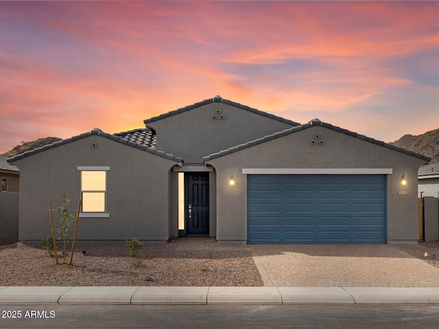 ranch-style home featuring decorative driveway, a tiled roof, an attached garage, and stucco siding
