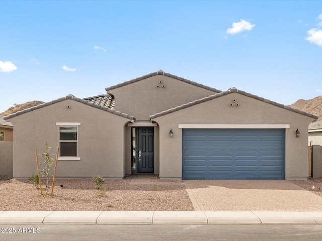 ranch-style house featuring decorative driveway, an attached garage, stucco siding, a tiled roof, and fence