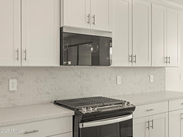 kitchen with stainless steel gas stove, light stone counters, white cabinets, and decorative backsplash