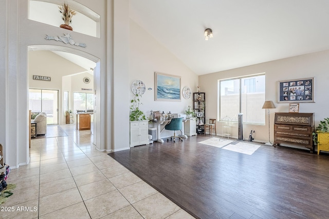 entrance foyer featuring high vaulted ceiling, arched walkways, a healthy amount of sunlight, and light wood finished floors