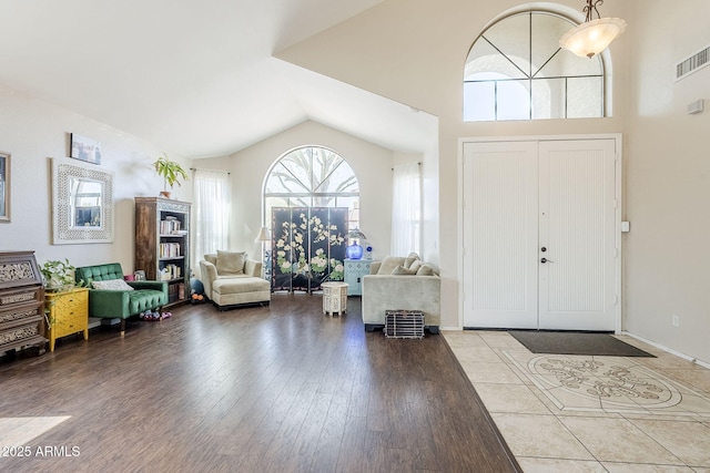 foyer entrance featuring high vaulted ceiling, visible vents, baseboards, and wood finished floors