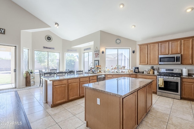 kitchen featuring light stone counters, a peninsula, a kitchen island, a sink, and appliances with stainless steel finishes