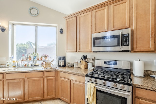 kitchen with light stone counters, vaulted ceiling, stainless steel appliances, light brown cabinetry, and a sink