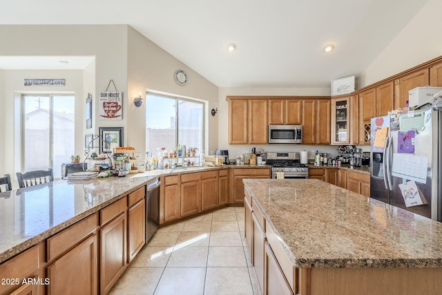 kitchen with stainless steel appliances, lofted ceiling, brown cabinetry, and light stone countertops