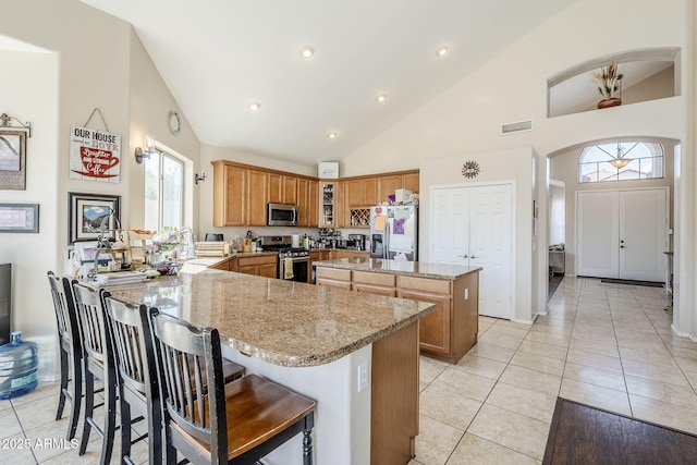 kitchen featuring visible vents, appliances with stainless steel finishes, a center island, a peninsula, and light stone countertops