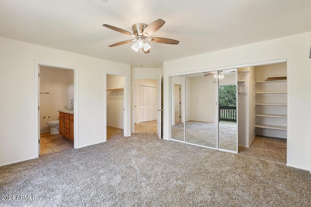 unfurnished bedroom with two closets, connected bathroom, light colored carpet, and ceiling fan