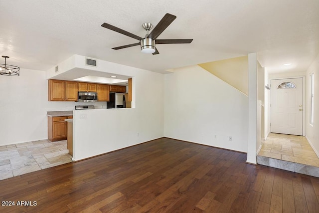 unfurnished living room with ceiling fan with notable chandelier and light hardwood / wood-style floors