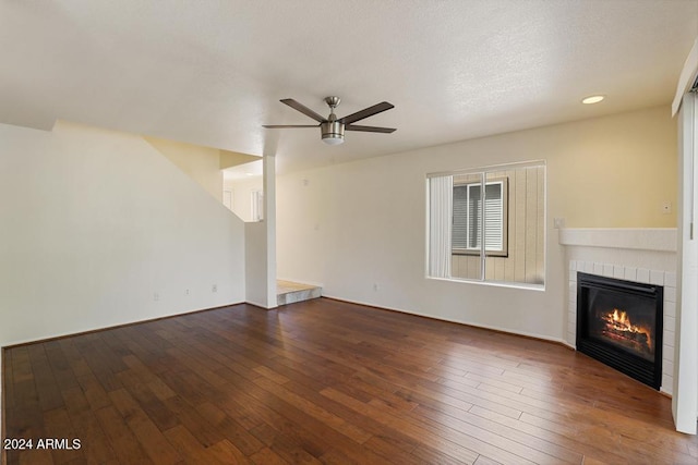 unfurnished living room featuring ceiling fan, dark wood-type flooring, and a tiled fireplace