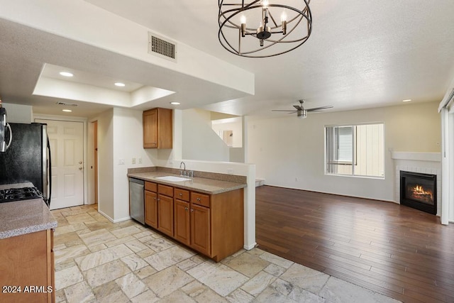 kitchen featuring ceiling fan with notable chandelier, sink, light wood-type flooring, stainless steel appliances, and a tiled fireplace