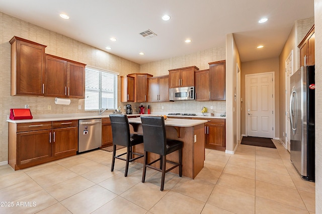 kitchen with stainless steel appliances, a kitchen island, visible vents, light countertops, and a kitchen bar