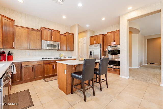 kitchen with light tile patterned floors, brown cabinetry, a kitchen island, appliances with stainless steel finishes, and a breakfast bar