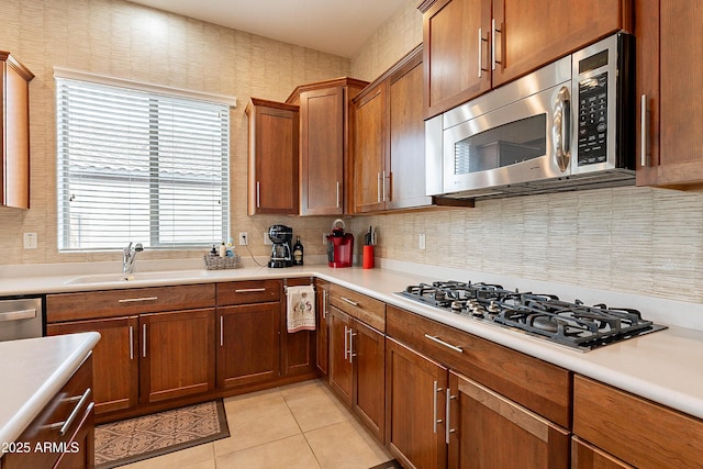 kitchen featuring light tile patterned floors, stainless steel appliances, a sink, light countertops, and brown cabinetry