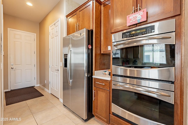 kitchen featuring light tile patterned floors, appliances with stainless steel finishes, brown cabinetry, and baseboards