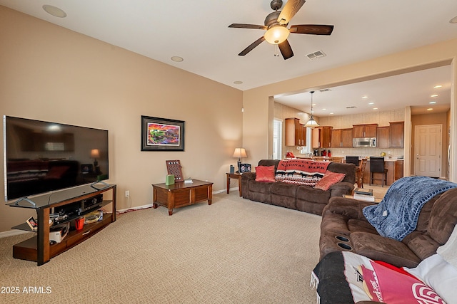 living area with baseboards, a ceiling fan, visible vents, and light colored carpet