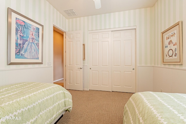 carpeted bedroom with wallpapered walls, a closet, visible vents, and a wainscoted wall