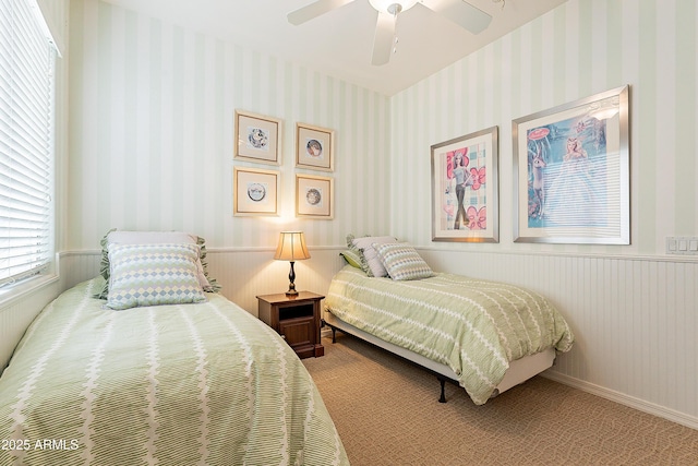 carpeted bedroom featuring wallpapered walls, ceiling fan, baseboards, and a wainscoted wall