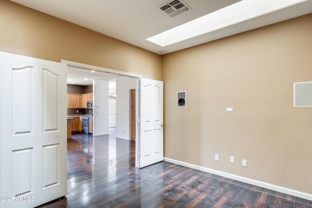 unfurnished room with a skylight, baseboards, dark wood finished floors, and visible vents
