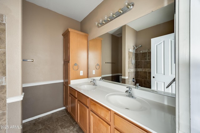 bathroom featuring a tile shower, double vanity, a sink, and baseboards